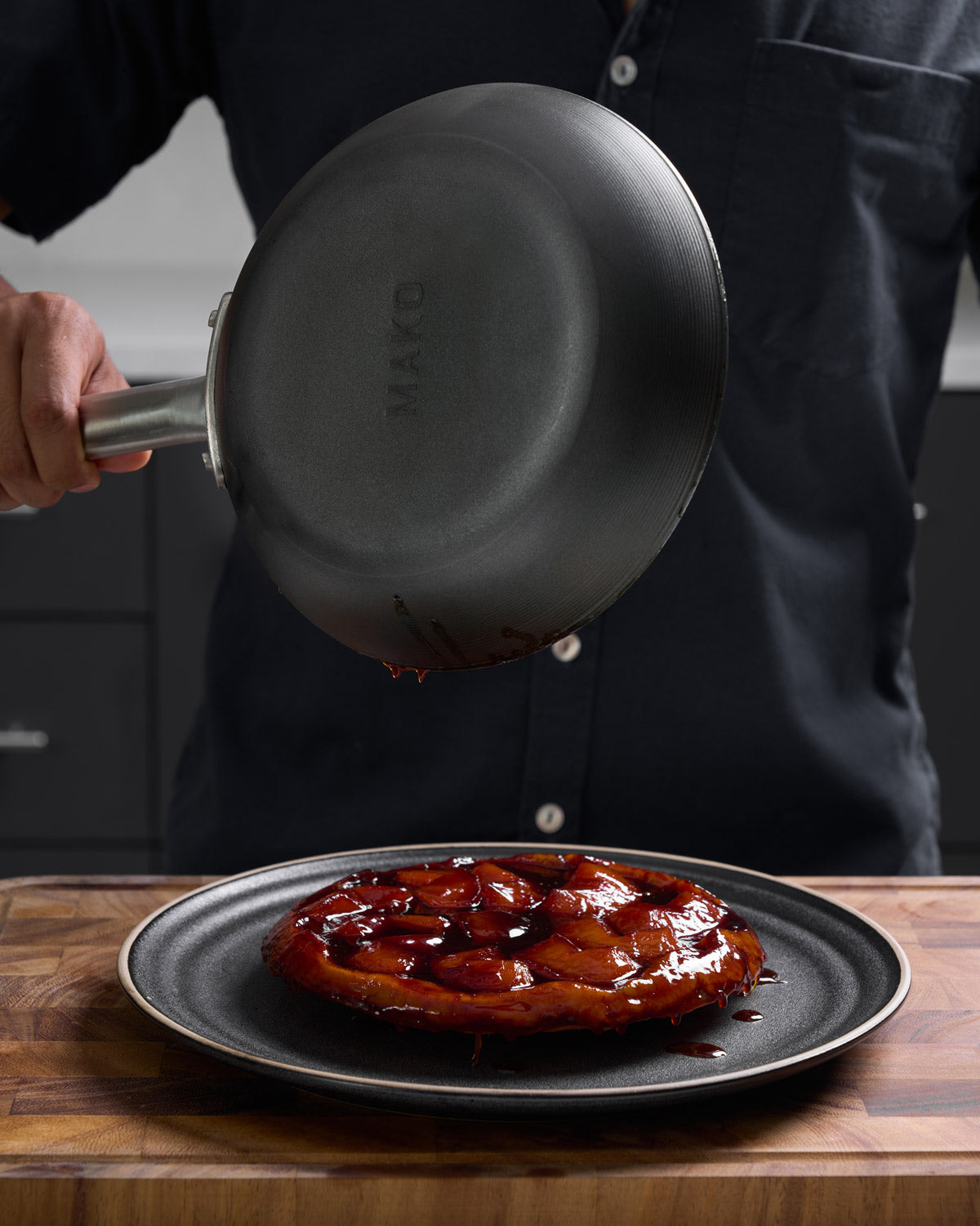 Black steel frying pan turning out caramelized tart onto plate on wooden board