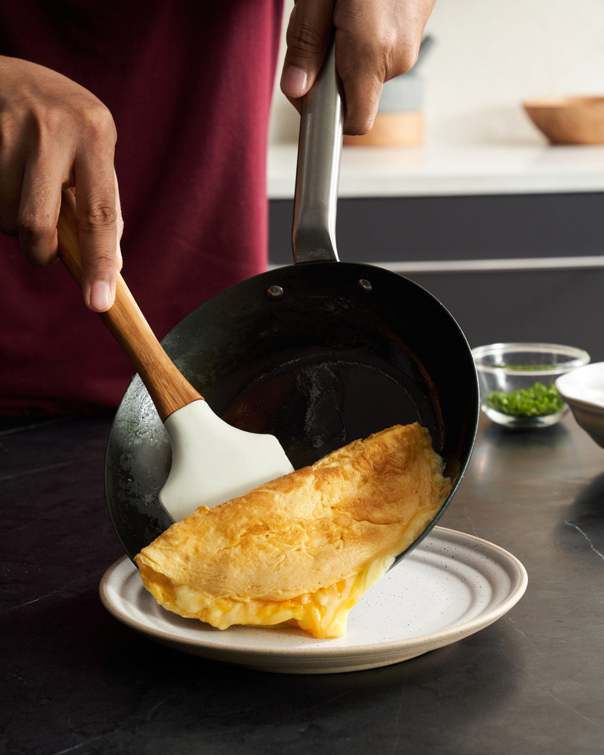 Person serving an omelette from a black steel frying pan onto a plate in a modern kitchen