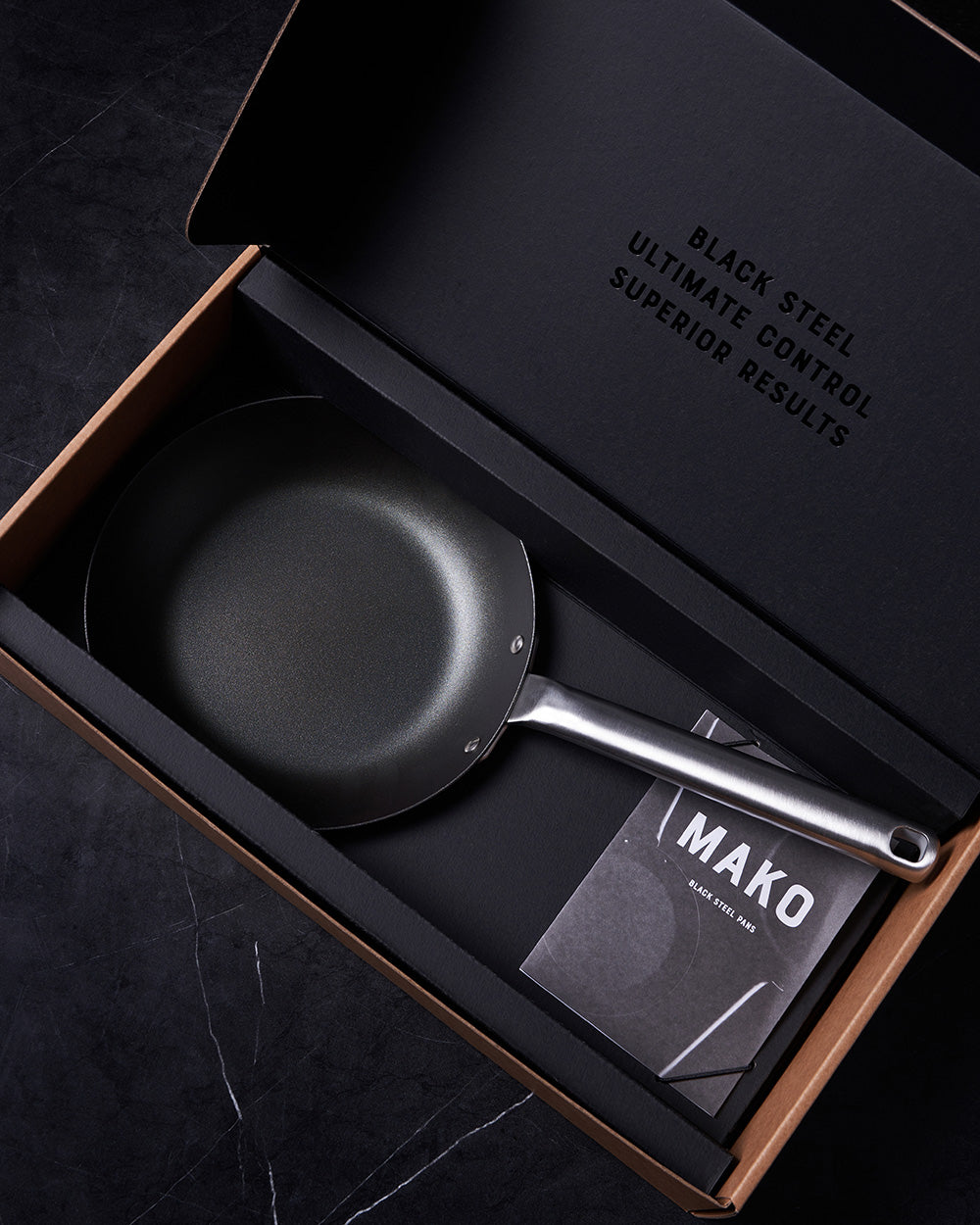 Black steel frying pan with silver handle in gift box on dark marble surface