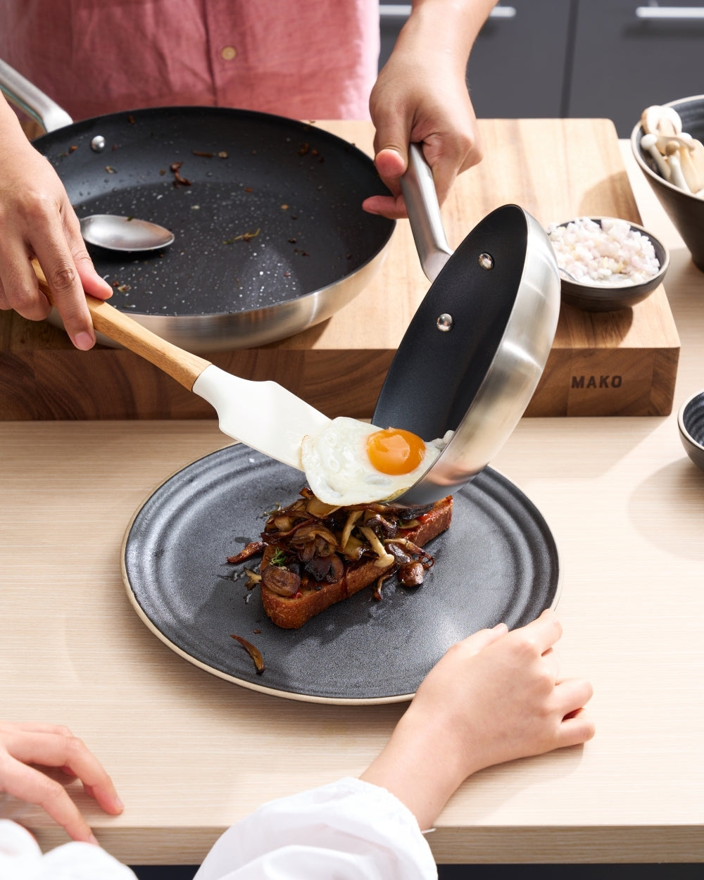 Non-stick frying pan serving a fried egg onto toast with sautéed vegetables on a plate