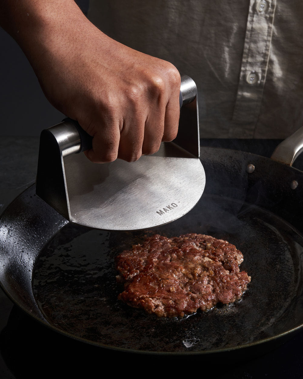 Hand pressing a burger patty on a skillet with a stainless steel burger press