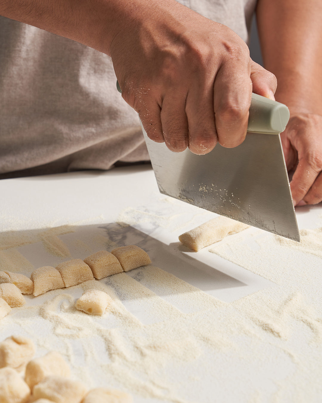 Hand using a dough scraper to cut homemade pasta on a floured kitchen surface