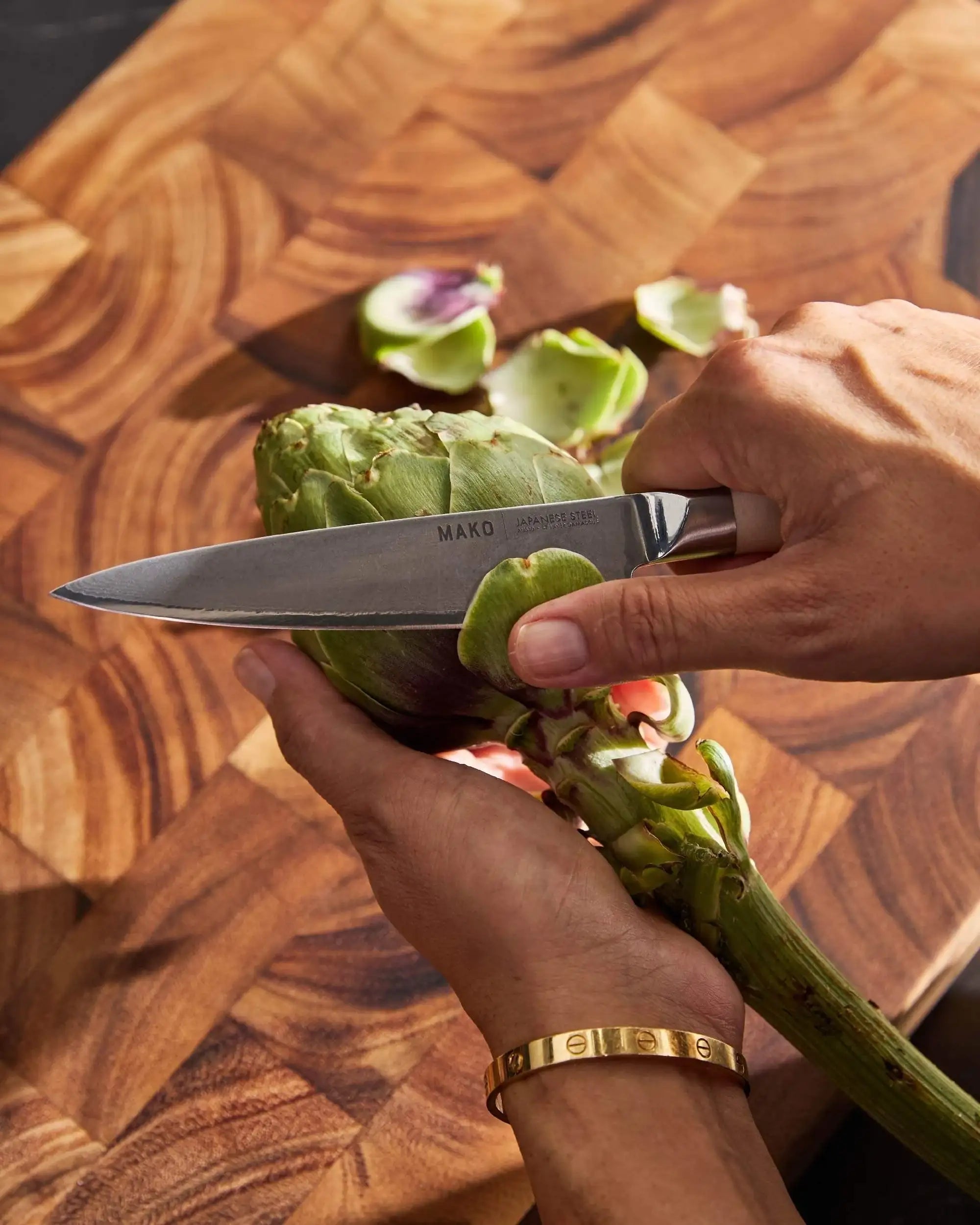 Hands peeling artichoke with Mako Japanese steel utility knife on wooden cutting board