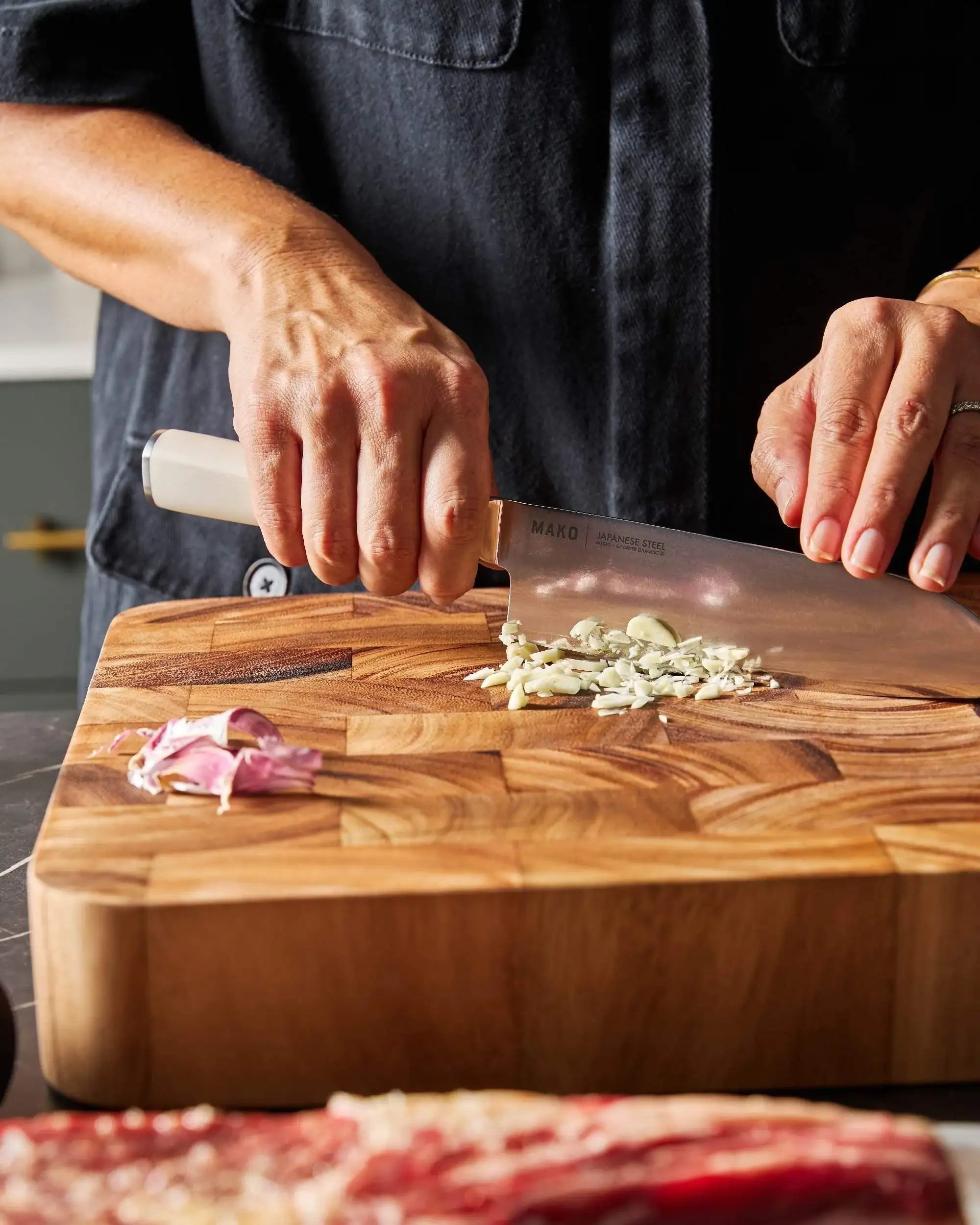 Hands chopping garlic with a Mako Japanese steel Santoku knife on a wooden cutting board