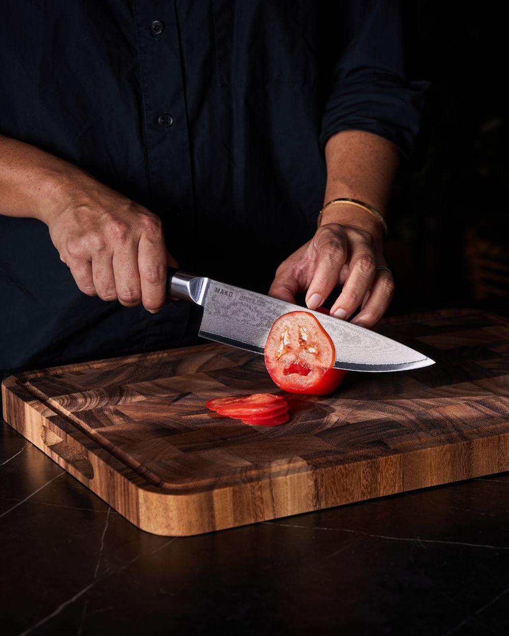 Person slicing tomato with Japanese steel chef knife on wooden cutting board