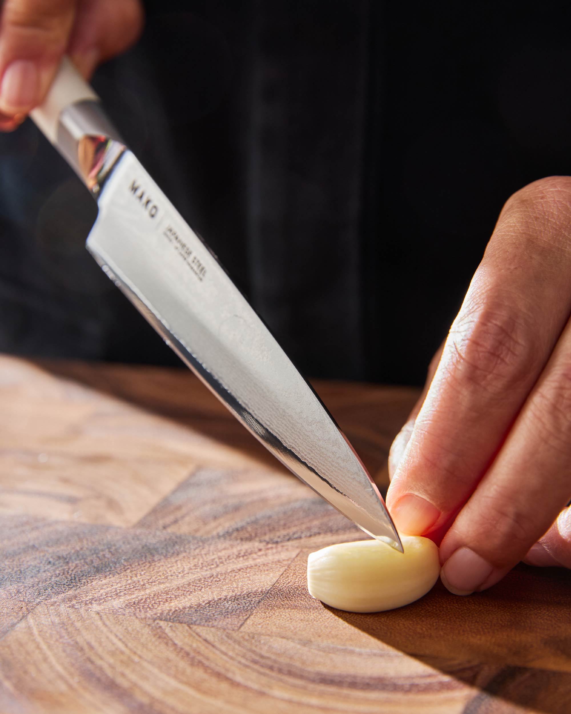 Japanese steel kitchen knife slicing garlic clove on wooden cutting board
