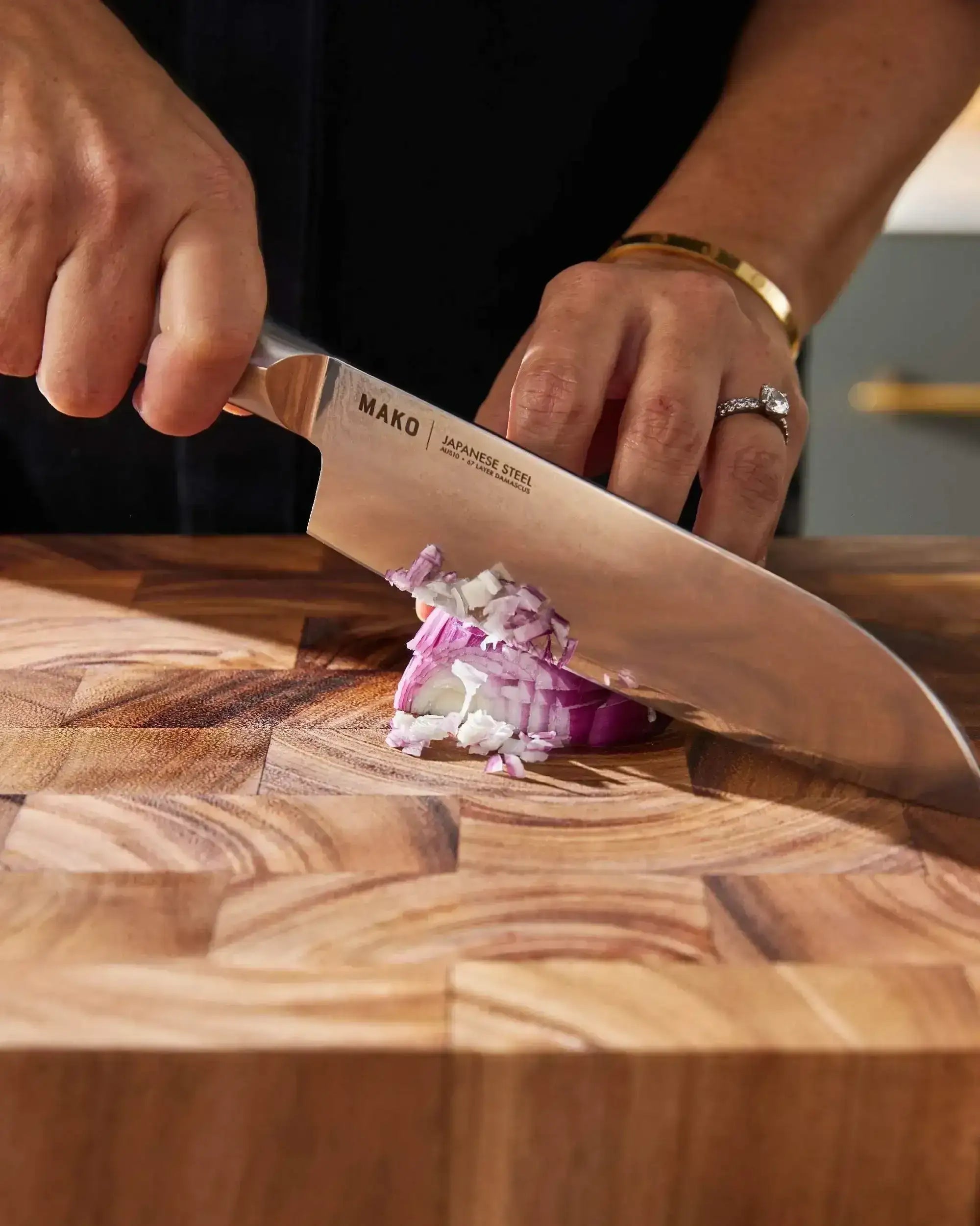 Mako Japanese steel knife slicing red onion on wooden cutting board, Marion Grasby endorsed
