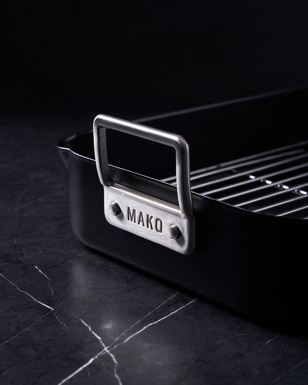 Non-stick black roaster pan with metal handle and rack on dark marble surface