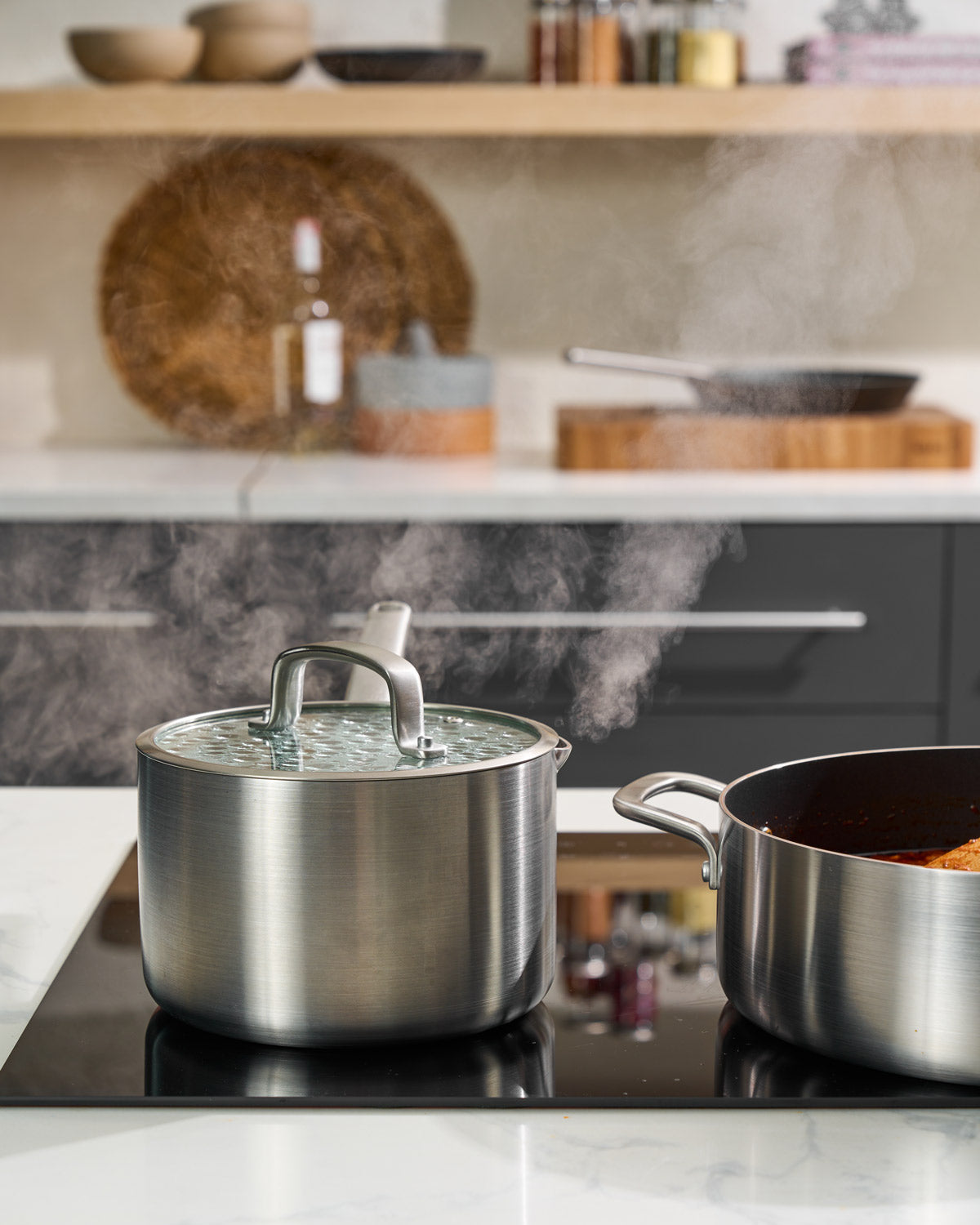 Stainless steel saucepan with glass lid steaming on modern kitchen stovetop