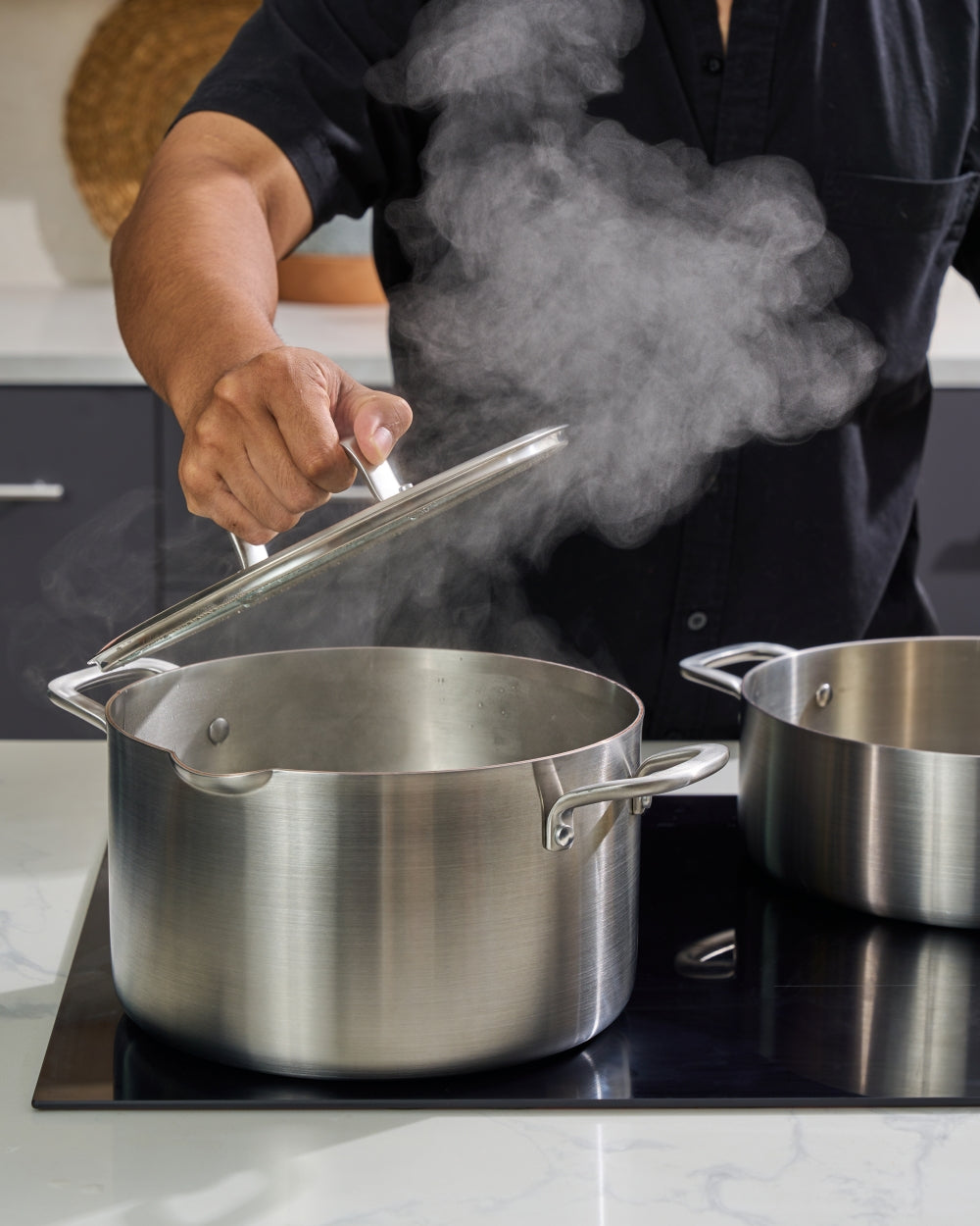 Person lifting lid from stainless steel stock pot with steam on kitchen stovetop