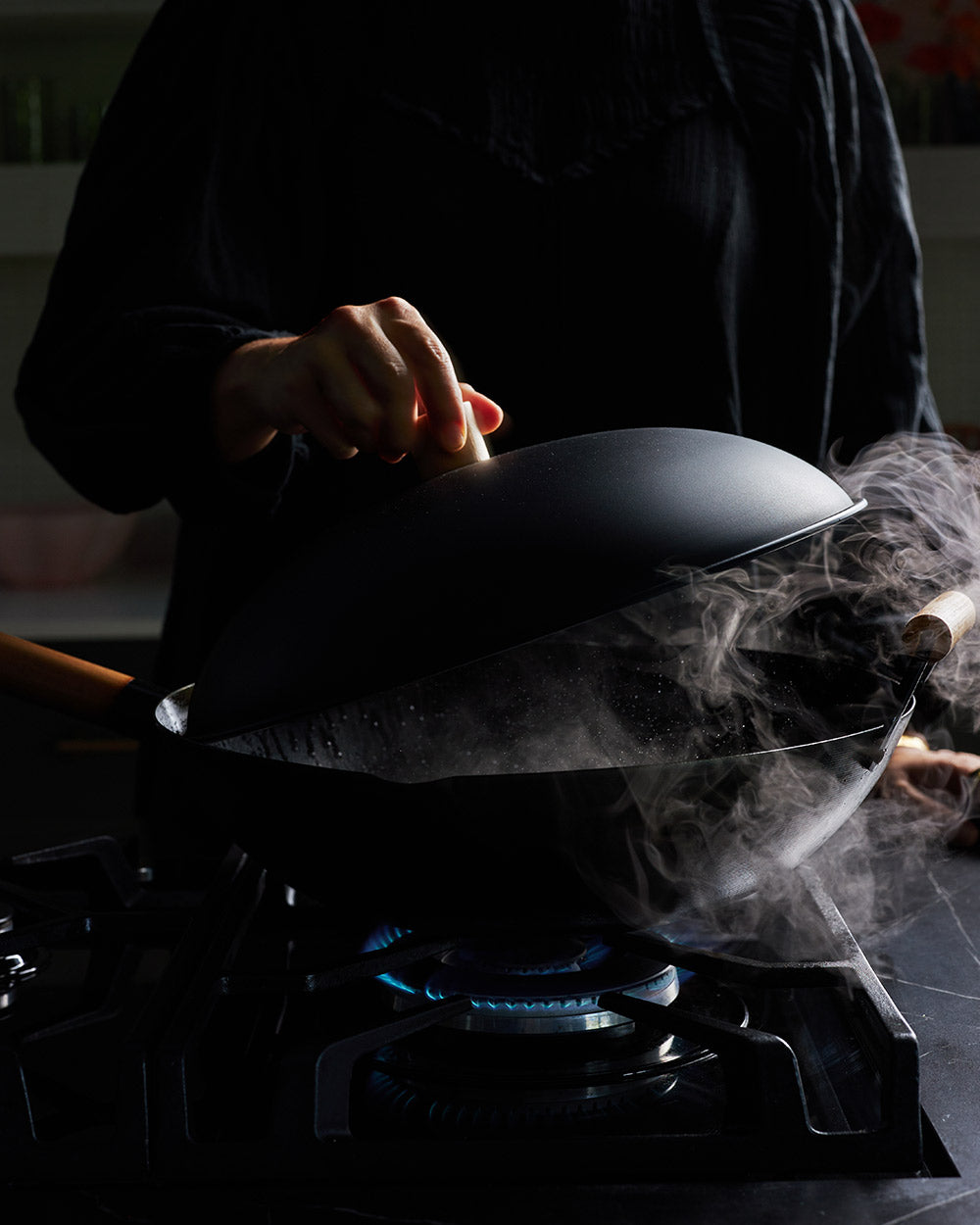Person lifting lid off speckled wok with steam rising, cooking on gas stove
