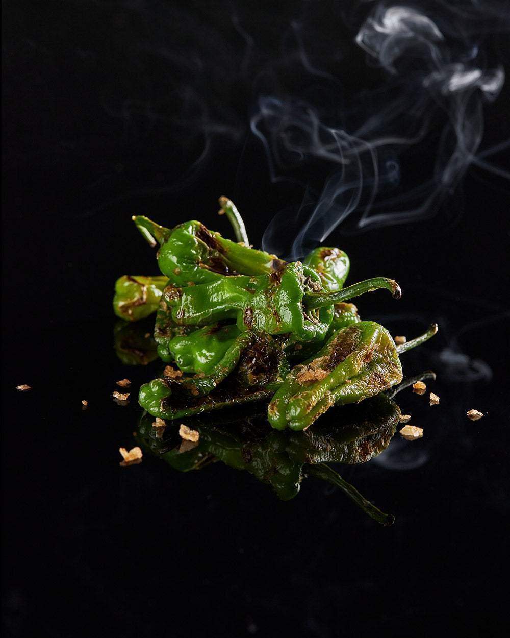 Charred green peppers with smoky steam on black reflective surface, photo by Marion Grasby