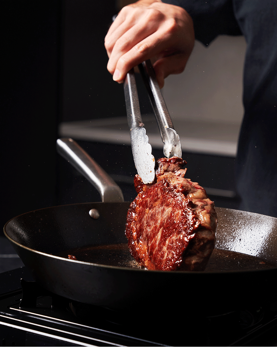 Person searing a steak in MAKO Steak Pan with tongs