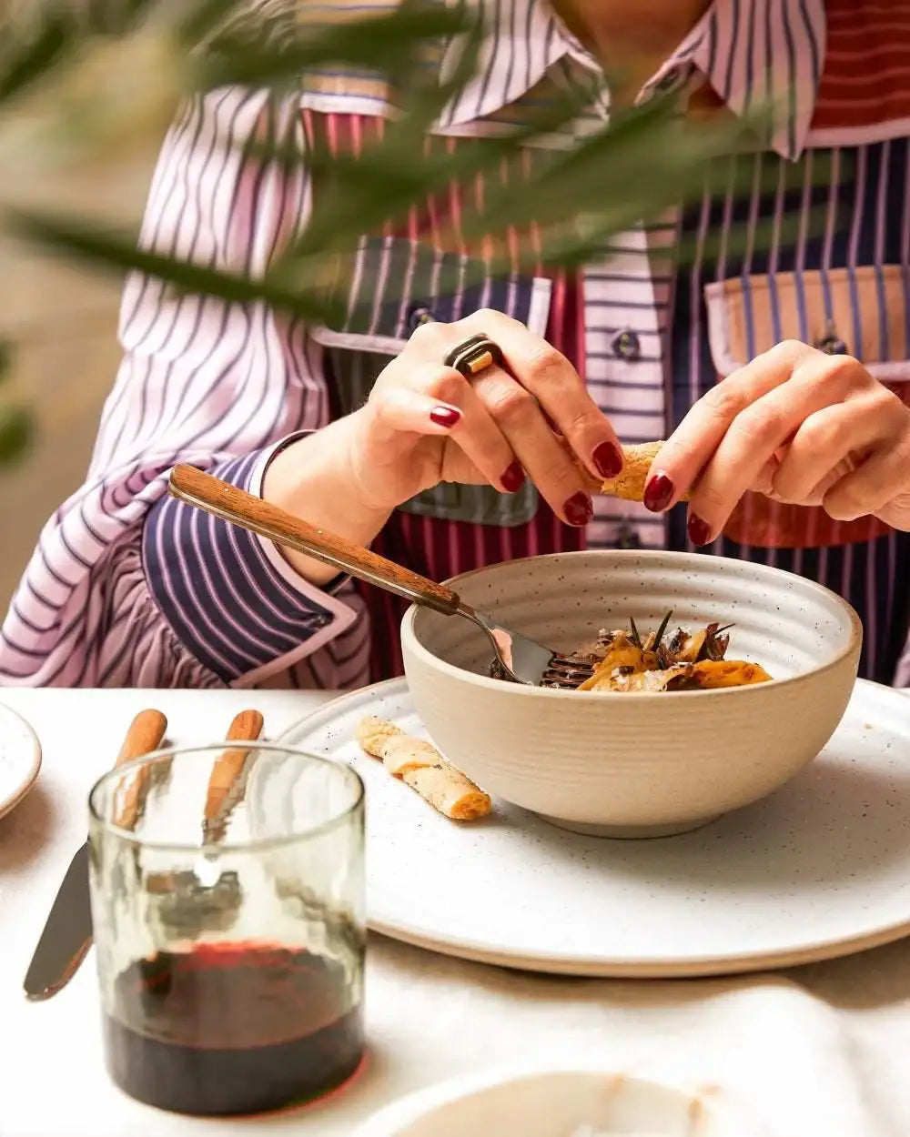 Person with manicured red nails breaking bread over a beige Asoke ceramic bowl set by Marion Grasby