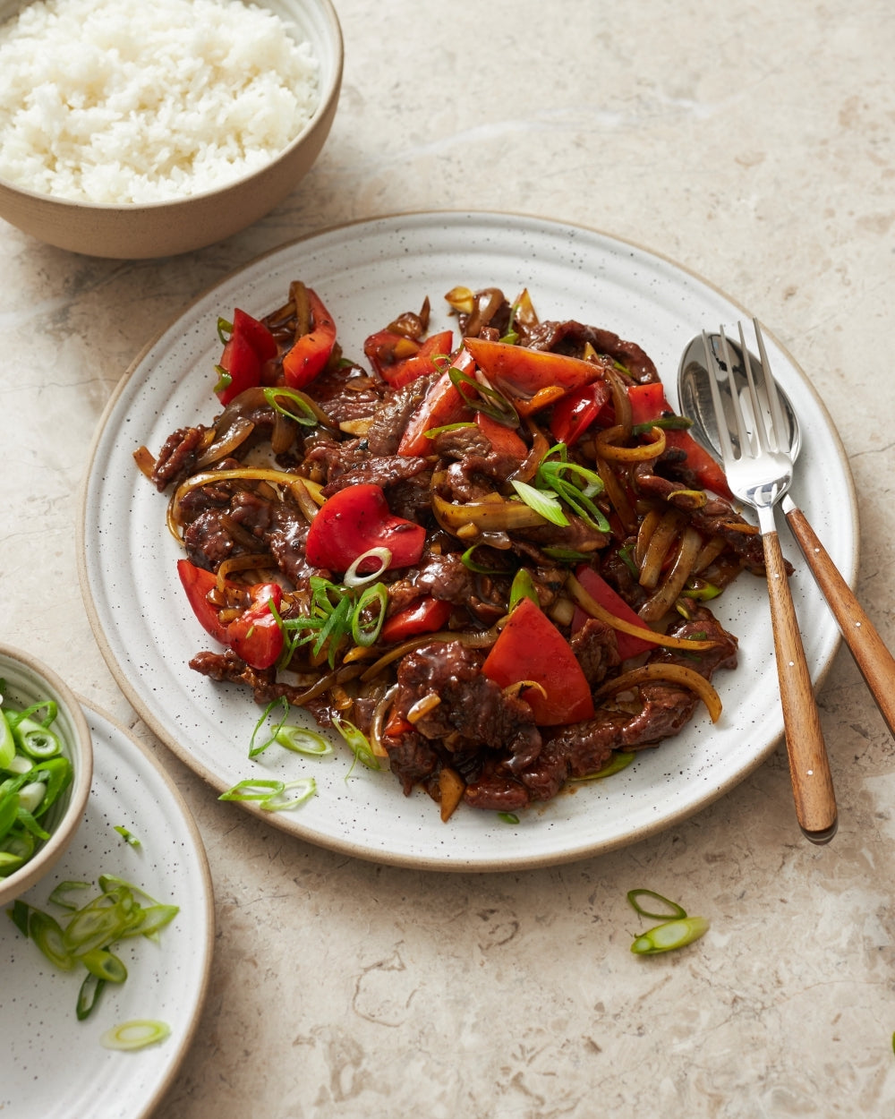 Set of speckled ceramic dinner plates with a stir-fry meal and sides on a stone surface