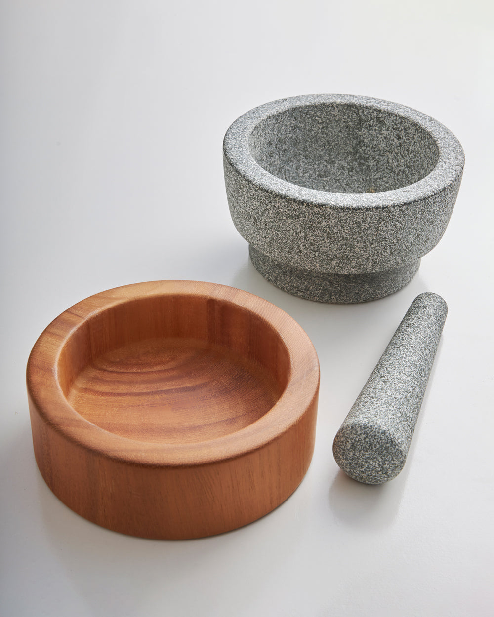 Granite mortar and pestle set with wooden spice bowl on white background.