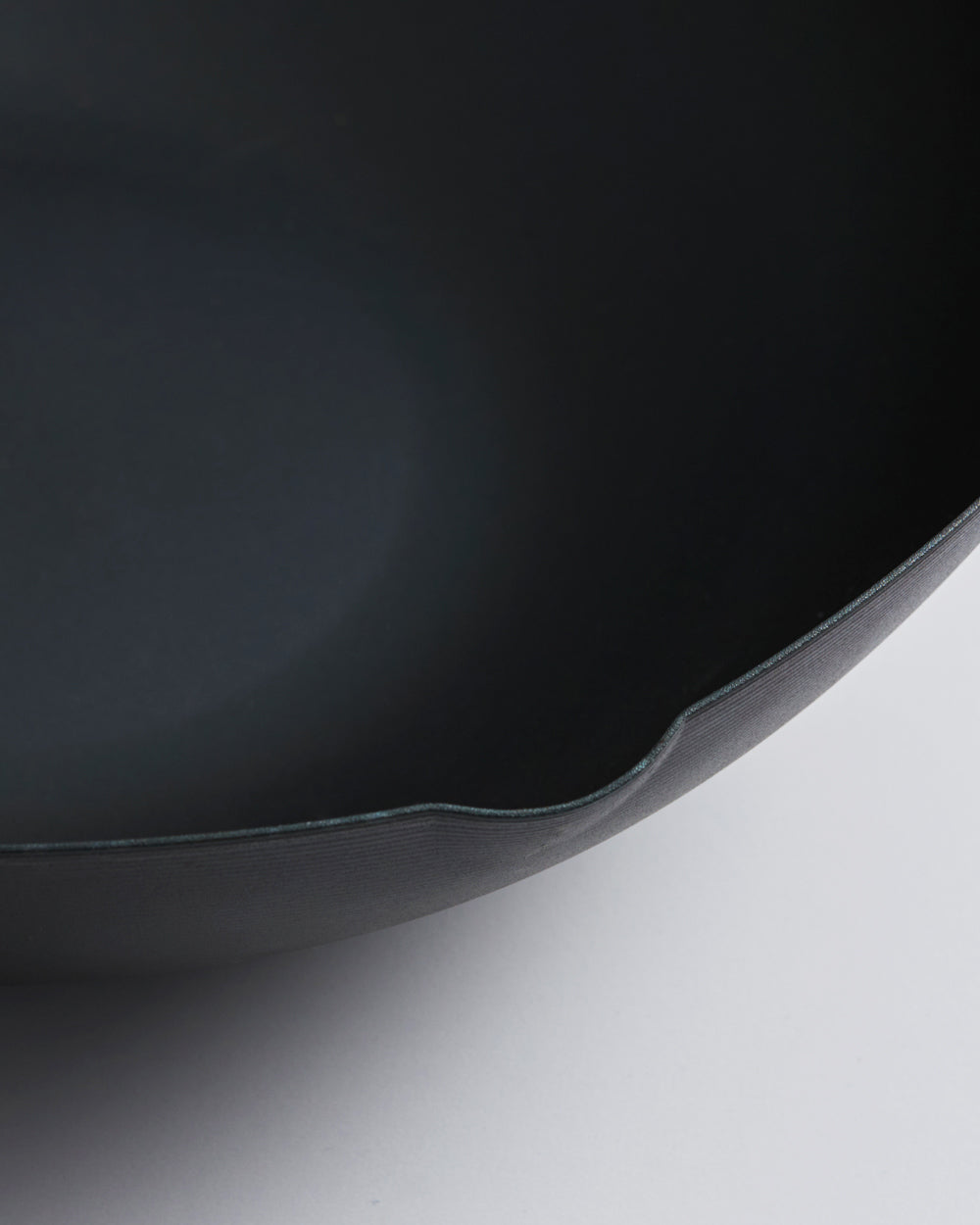 Close-up of black steel wok edge, matte finish, curved lip on light background