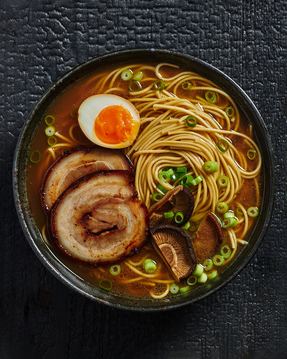 Bowl of ramen with sliced pork, soft-boiled egg, mushrooms, scallions, and noodles in broth